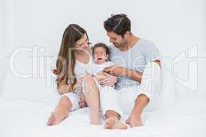 Parents with crying baby sitting on bed