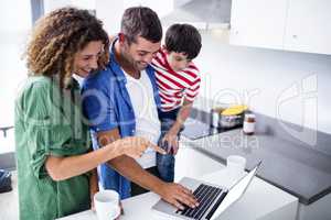 Parents using laptop with son in kitchen