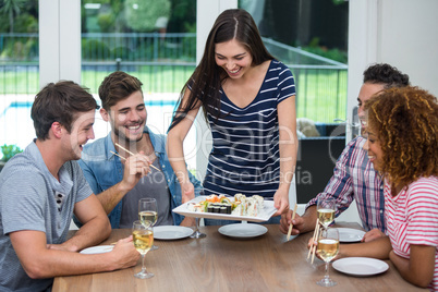 Woman serving sushi to friends while drinking wine