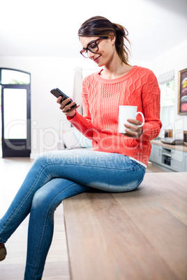 Young woman with mobile phone and mug sitting on table