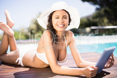 Portrait of happy woman in hat using digital tablet by pool side