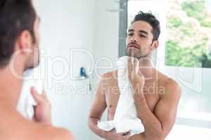 Young man wiping face while looking in mirror