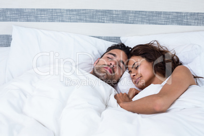 Couple with eyes closed while relaxing on bed