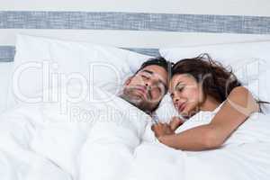 Couple with eyes closed while relaxing on bed