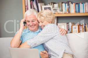 Excited senior woman hugging her husband while using laptop