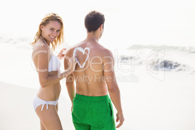 Woman making a heart symbol on mans back while applying a sunscr