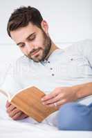 Man reading book on bed at home