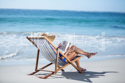 Pretty mature woman reading a book lying on deck chair