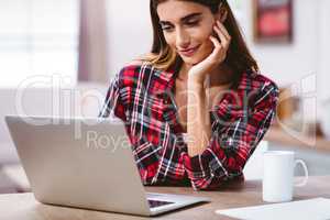 Smiling woman using laptop with hand on chin