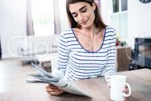 Young woman with newspaper and mug