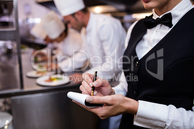 Close-up of waitress with note pad in commercial kitchen