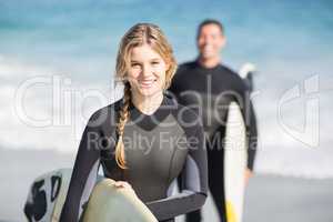 Happy woman in wetsuit holding a surfboard on the beach