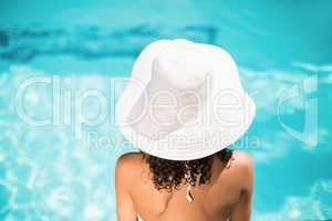 Rear view of woman in white hat sitting near pool