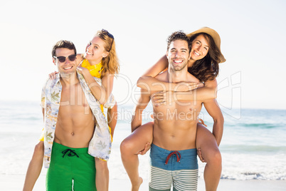 Two men giving a piggy back to women on the beach