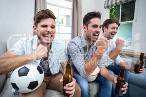Cheerful male friends watching soccer match on TV