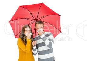 Young couple holding umbrella and wiping nose