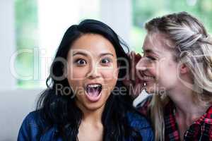 Happy young woman whispering to female friend