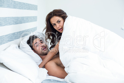Surprised young couple enjoying on bed