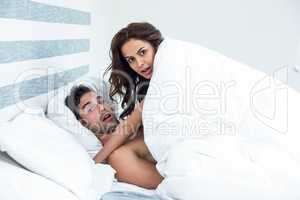 Surprised young couple enjoying on bed