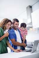 Parents using laptop with son in kitchen