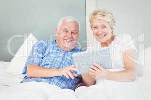 Portrait of senior couple using tablet on bed