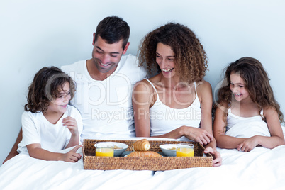 Happy family sitting with breakfast tray on bed