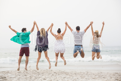Rear view of friends holding hands and jumping on the beach