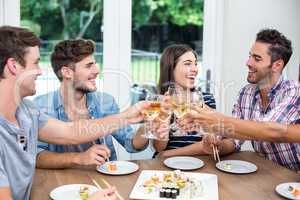 Cheerful friends toasting wine while having sushi