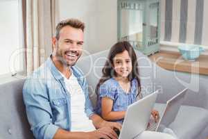 Father and daughter using laptop while sitting on sofa