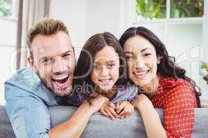 Happy parents with daughter on sofa at home