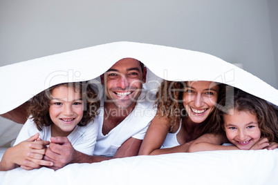 Portrait of happy family lying under a bedsheet