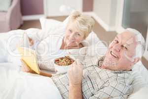 Portrait of couple reading book while having breakfast on bed
