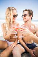 Young couple in sunglasses toasting cocktail glass on the beach