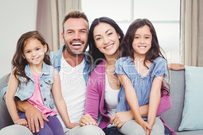 Portrait of parents sitting with daughters on sofa