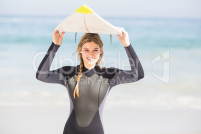 Portrait of woman in wetsuit carrying surfboard over head