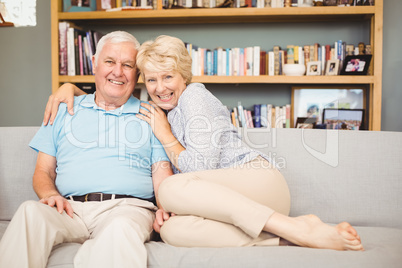 Portrait of happy senior couple sitting on sofa against bookshel