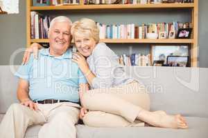Portrait of happy senior couple sitting on sofa against bookshel