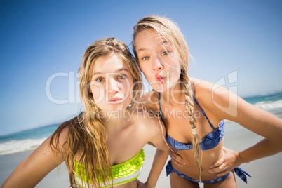 Two happy women standing on the beach with hand on hip