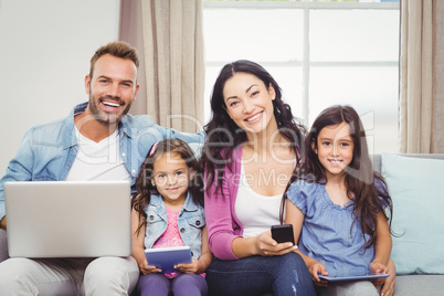 Happy family using modern technologies while sitting on sofa
