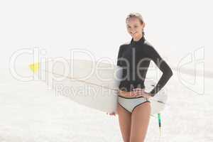 Woman in wetsuit holding a surfboard on the beach