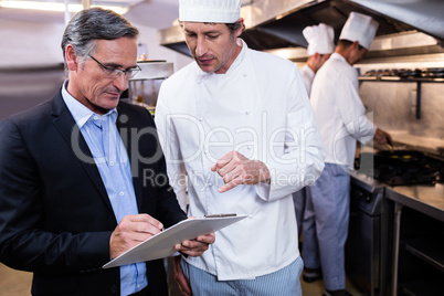 Male restaurant manager writing on clipboard while interacting t