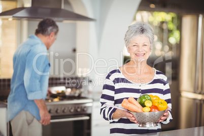 Portrait of happy senior woman holding colander with vegetables
