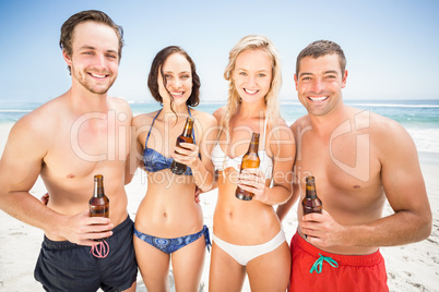 Portrait of happy friends standing on the beach with beer bottle