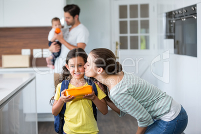 Mother kissing daughter wearing school bag