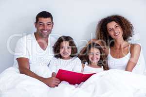 Portrait of family reading book together on bed