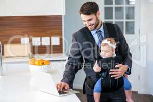 Businessman using laptop while carrying baby girl