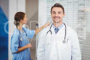 Portrait of smiling doctor with colleague pointing at chart