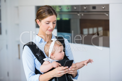 Woman using mobile phone while carrying baby girl