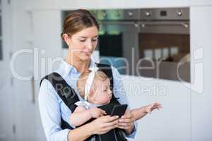 Woman using mobile phone while carrying baby girl