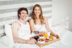 Portrait of young couple having breakfast on bed